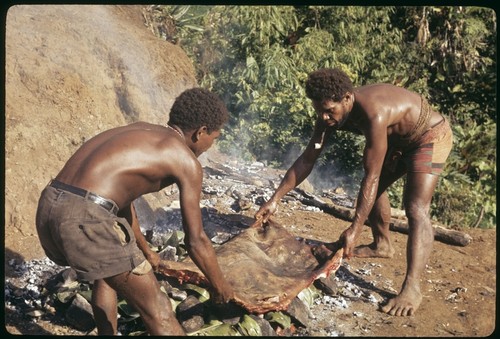 Two men laying pork out on the stone oven