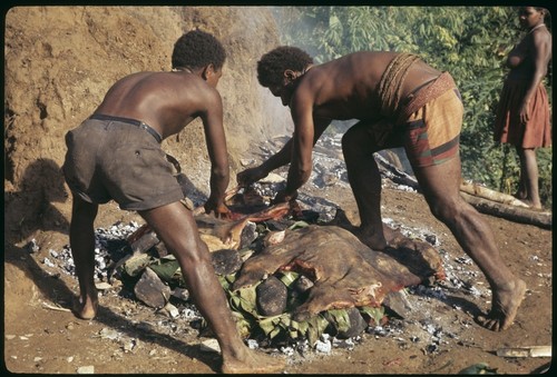 Two men laying pork out on the stone oven