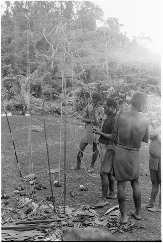 Men standing with shell money valuables on poles ready for presentation at mortuary feast