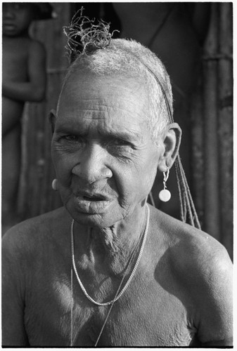 An elderly Kwaio woman, her woven 'purse' over her head, wearing shell earrings