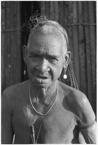 An elderly Kwaio woman, her woven 'purse' over her head, wearing shell earrings