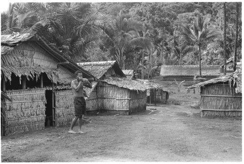 Man blowing a conchshell horn in what appears to be a coastal Christian village, likely not in Kwaio