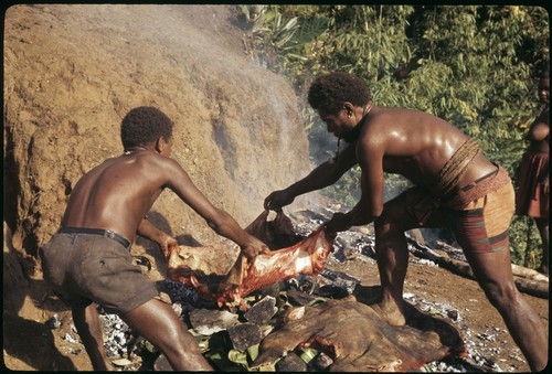 Two men laying pork out on the stone oven