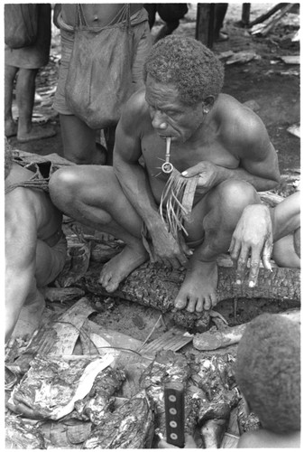 Feastgiver supervises the carving of pork portions for his guests, using strips torn on a leaf to keep track of the portions