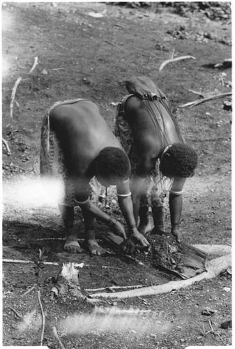 Two women scraping debris from the clearing into a bark "dustpan"