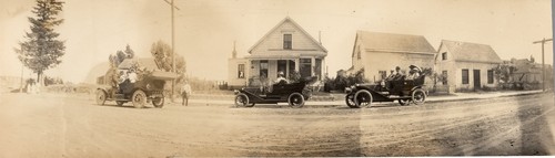 Trio of touring cars pausing on the road in front of houses