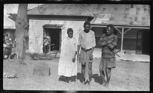 Two men and a woman in torn clothes, outside a building