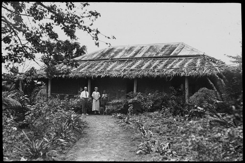 European man and woman, with female native in front of house