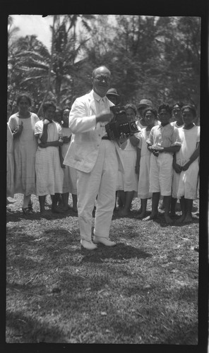 Lambert holding a camera, in front of a group of Cook Islanders