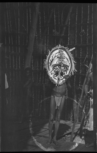 Kaimari village man wearing a mask, standing by a fire pit inside a house