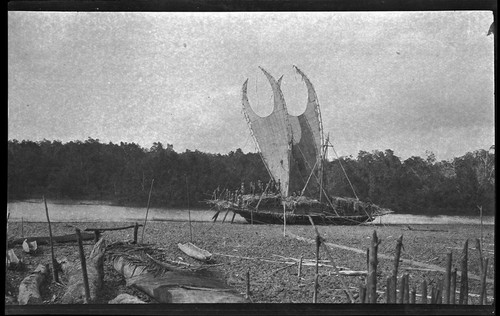 Large lakatoi canoe with people on board, on mudflat