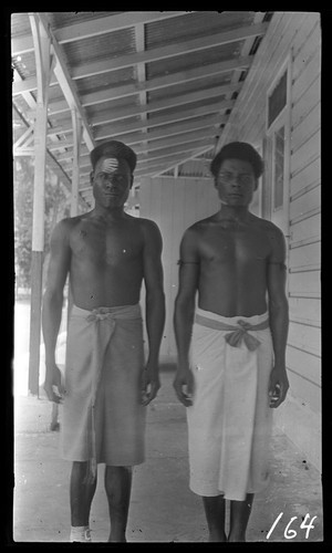 Two men outside a building, one with forehead marking