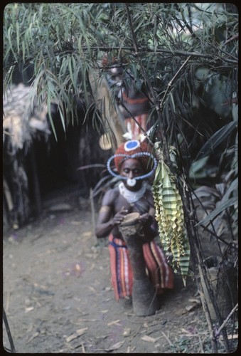 Pig festival, wig ritual: Akis with red wig (mamp gunc) beats on drum, folded cordyline leaf ornament in foreground