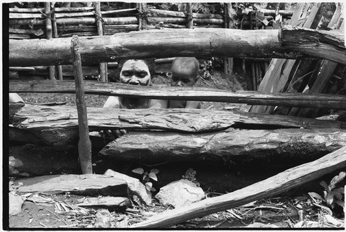 Bomagai: woman, wearing clay as sign of mourning, and young child peer through fence