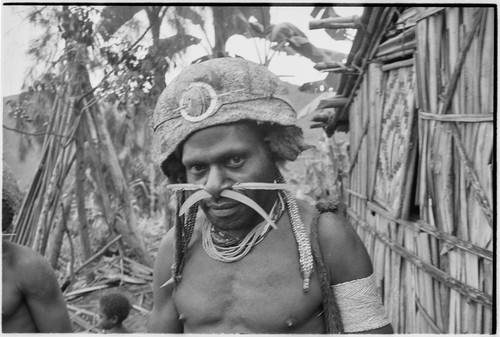 Young man wears adornments, including barkcloth cap and trade-bead necklace by Rappaport's house