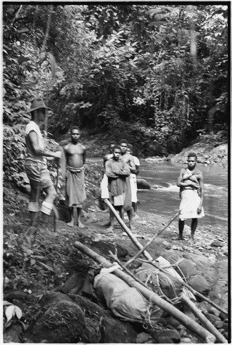 Carriers and Pete Vayda with cargo tied to poles beside a river