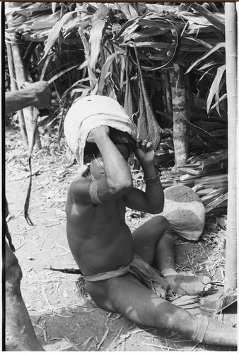 Pig festival, wig ritual, Tsembaga: in preparation for red wig construction, man removes barkcloth cap, his hair has not been cut since childhood