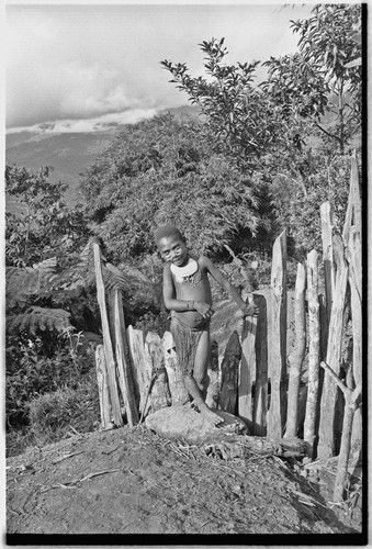 Young girl wearing shell valuables stands by a fence