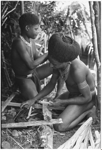 Pig festival, wig ritual, Tsembaga: man with wig frame in hair prepares a fire