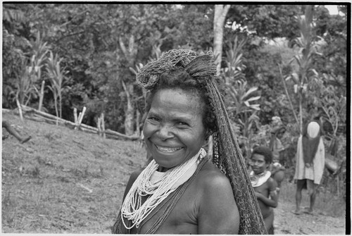 Smiling woman with beaded necklace and shell valuable, carries netbag slung from her head