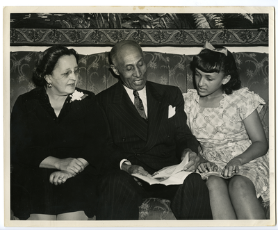 Pearl H. Roberts, Frederick M. Roberts, and Patricia Roberts sitting on sofa looking at documents