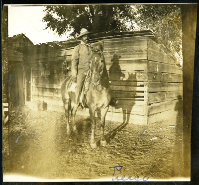 Black cowboy riding a horse next to farm shed