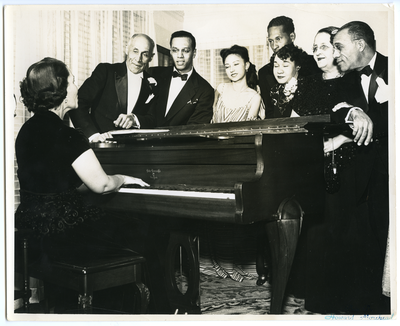 Group of men and women in evening attire standing at piano