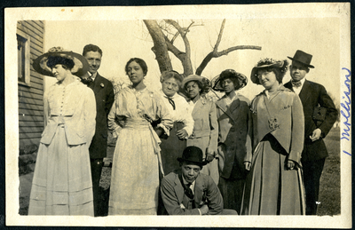 Nine men and women standing next to house