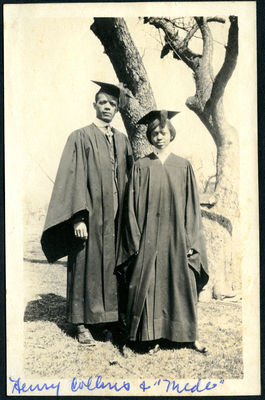 Man and woman in cap and gown standing next to tree