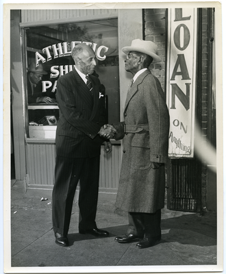 Frederick M. Roberts shaking hands with man in front of pawn shop