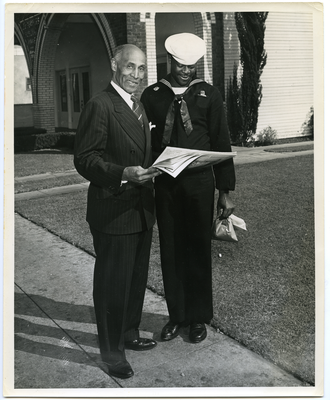 Frederick M. Roberts standing next to sailor looking at newspaper