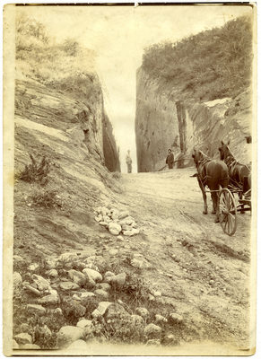 Dirt road with two horses pulling a carriage with men in the background standing looking in the direction of the camera