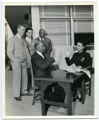 Frederick M. Roberts and Lena Horne sitting at a table with their right hands raised