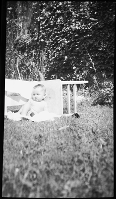 Baby sitting next to chair in yard