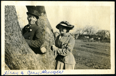 Pearl Hinds and man in suit and top hot leaning next to tree