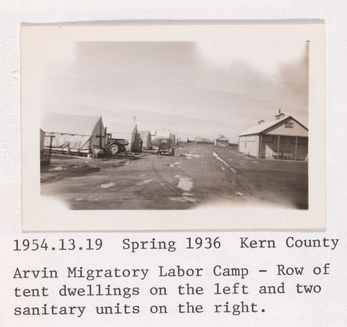 Spring, 1936, Kern County. Arvin Migratory Labor Camp - Row of tent dwellings on the left and two sanitary units on the right