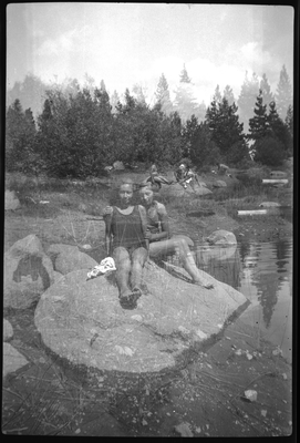 Two girls in swim suits sitting on boulder next to water