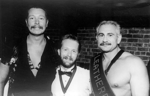 Three men posing for photograph, two wearing leather attire