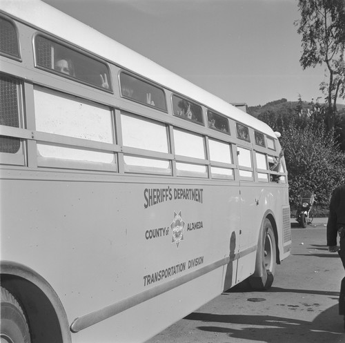 Girls in sheriff's bus holding V for victory with their hands out top of windows as bus leaves for jail