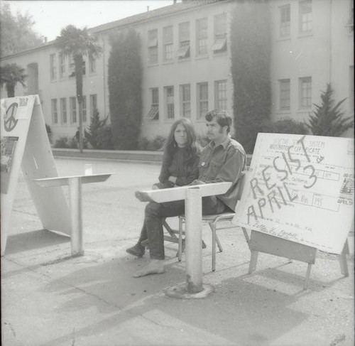 Two students sitting next to draft protest sign