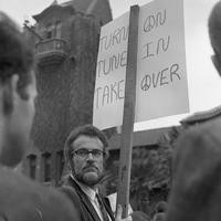 Man stands with protest sign on front of Tower Hall