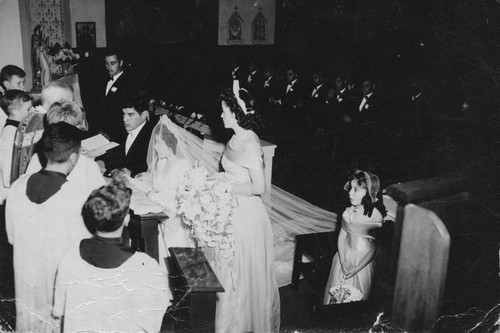 Attendants surround the priest and kneeling couple, Daniel Herrera and Lupe Ruiz during their wedding ceremony