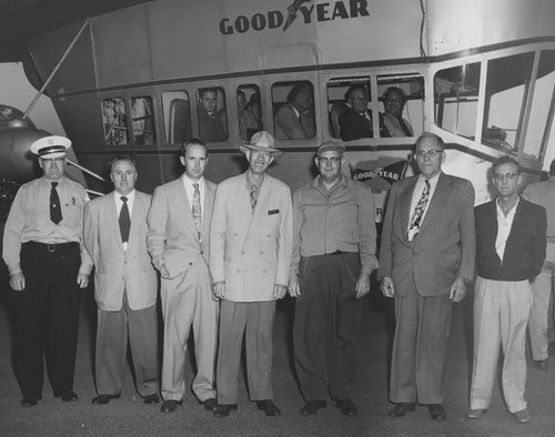 Group of men standing next to the Goodyear blimp