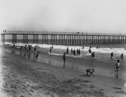 Beach scene at low tide with many bathers and a long pier in the background