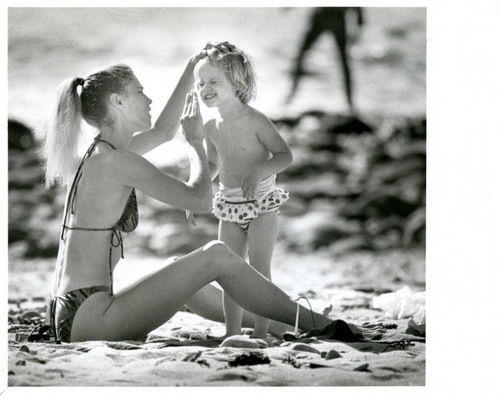 Mother applying sunscreen for her daughter on the beach, 1990s