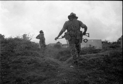 Armed soldiers walk through rough terrain, Guatemala, 1982