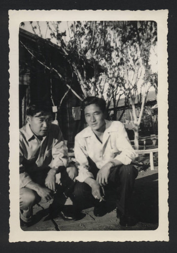 Two men crouching in front of clothes lines in Poston incarceration camp