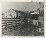 [Man and woman pose in corral at west end of deteriorating Santa Barbara Mission]