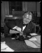 Los Angeles judge Leroy Dawson seated at desk playing with a portable phonograph, circa 1931