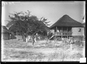 Swiss missionaries and African people in front of buildings with thatched roofs, Mozambique